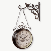 Antique double-sided wall clock with bird and cage motif on white wall